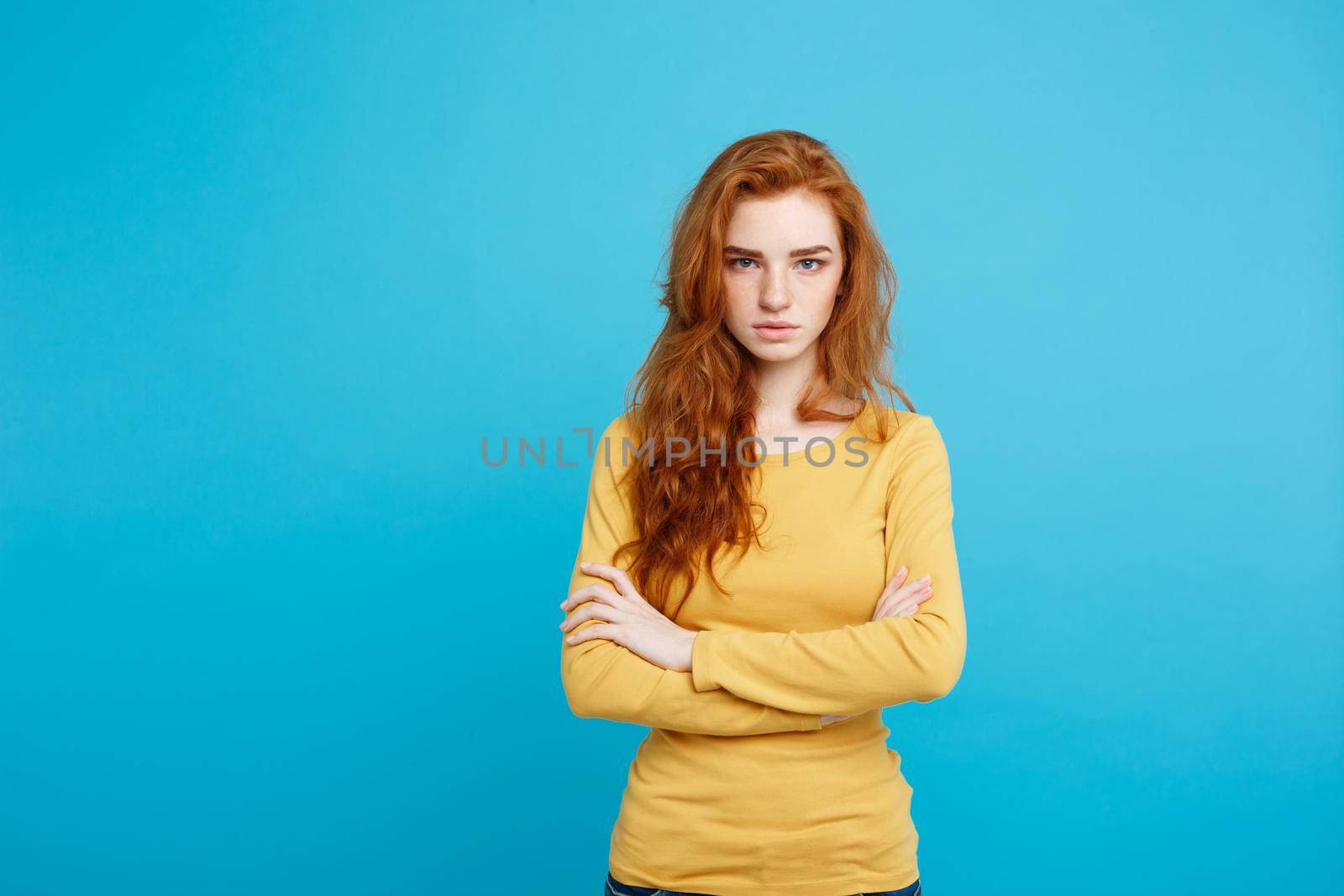 Portrait of young beautiful ginger woman with tender serious face crossing arms looking at camera. Isolated on pastel blue background. Copy space by Benzoix