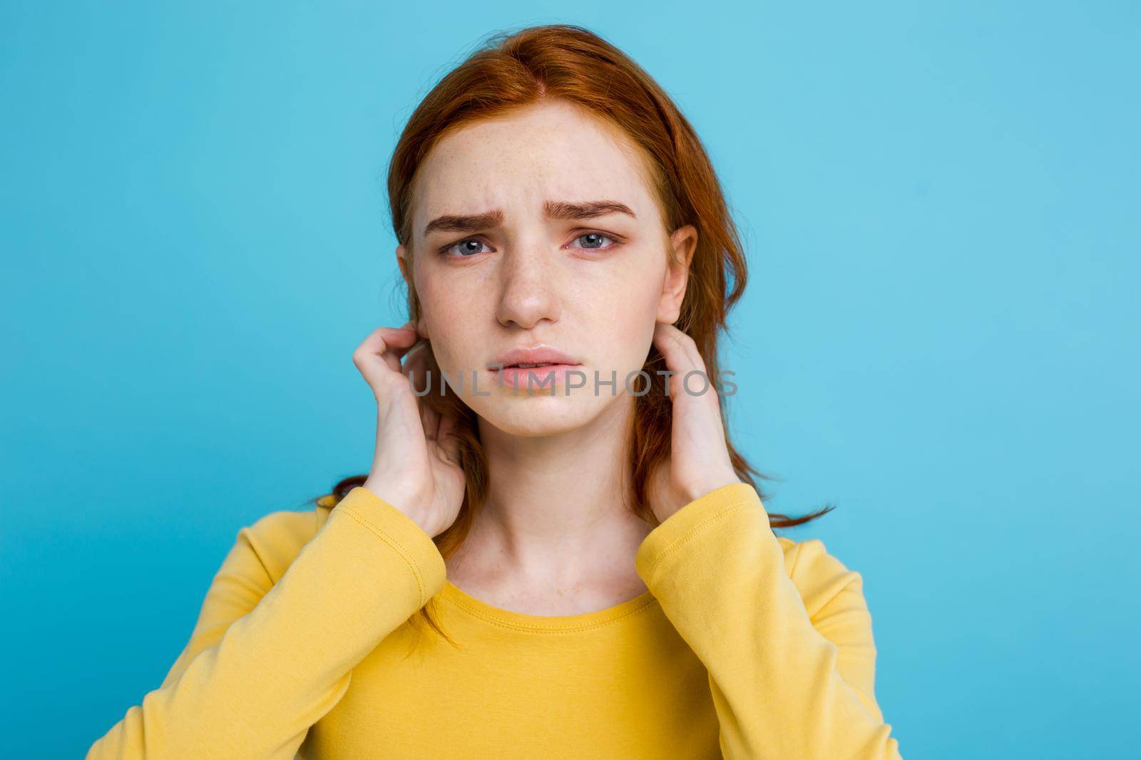 Headshot Portrait of tender redhead teenage girl with serious expression looking at camera. Caucasian woman model with ginger hair posing indoors.Pastel blue background. Copy Space.