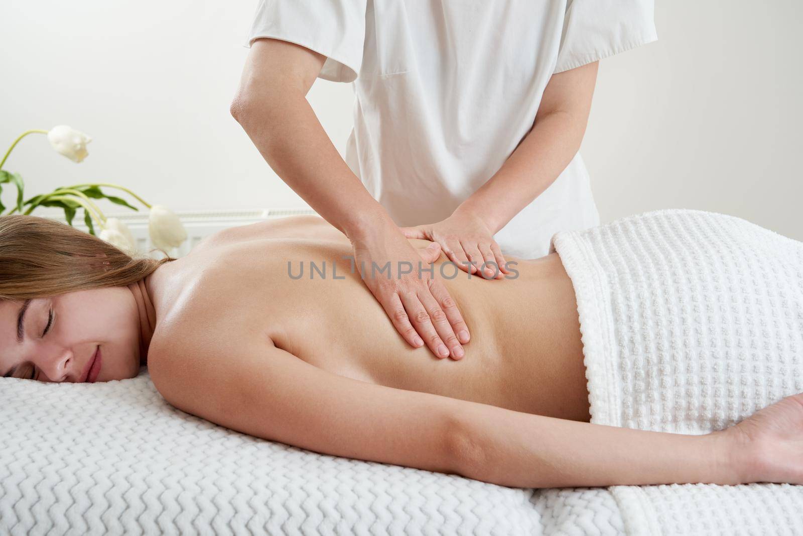 Masseur massaging young woman on massage table in a spa salon. Young woman relaxing during back massage at the spa. Spa treatment concept