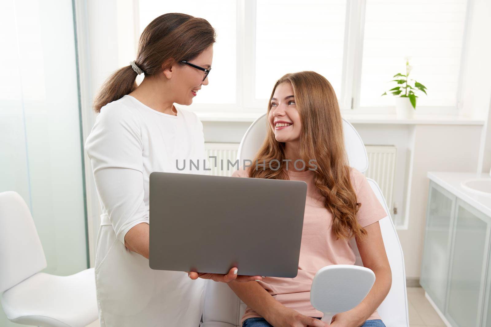 Cosmetologist working with patient while using laptop in clinic. Beauty doctor consults the patient. Cosmetologist and beauty surgeon concept by Mariakray