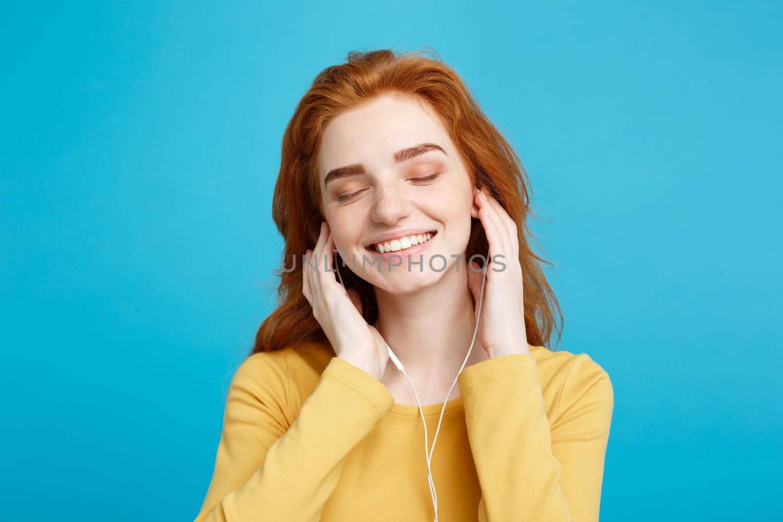 Lifestyle concept - Portrait of cheerful happy ginger red hair girl enjoy listening to music with headphones joyful smiling to camera. Isolated on Blue Pastel Background. Copy space. by Benzoix