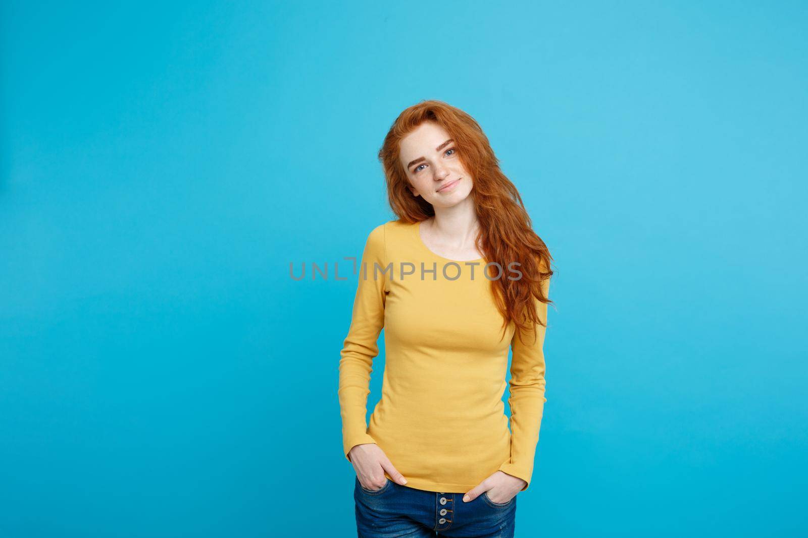 Portrait of young beautiful ginger woman with freckles cheerfuly smiling looking at camera. Isolated on pastel blue background. Copy space.