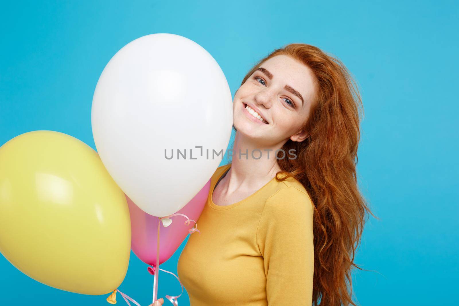 Close up Portrait happy young beautiful attractive redhair girl smiling with colorful party balloon. Blue Pastel Background.