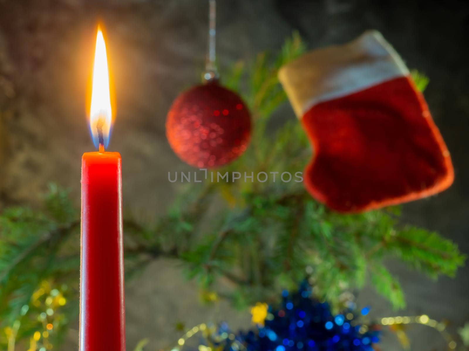 Christmas red candle burns against the background of fir branches.  by Puludi