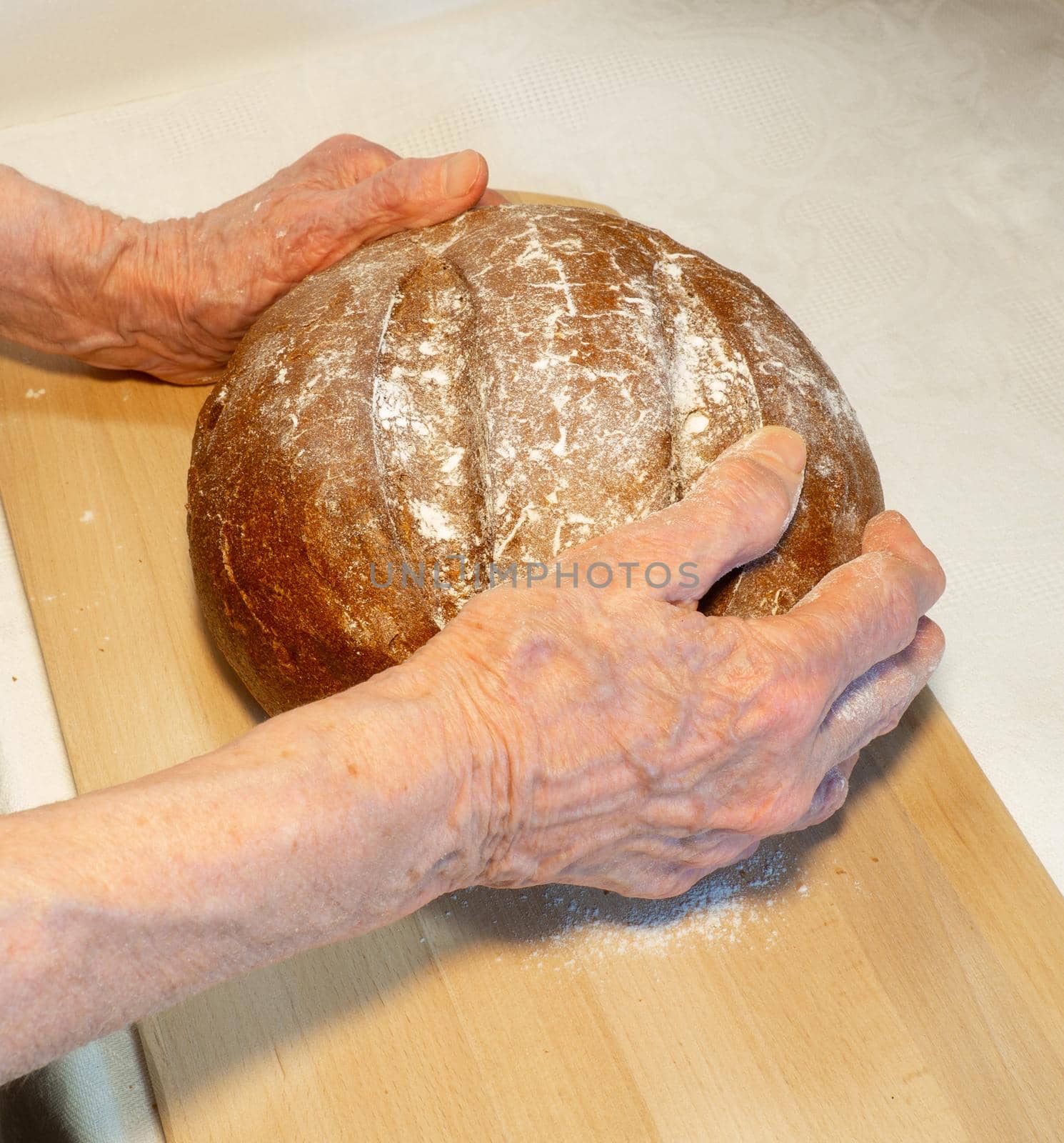 Black fresh round rye bread in the hands of an elderly man on the kitchen board. Bread in flour