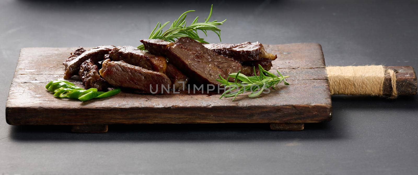 roasted piece of beef ribeye cut into pieces on a vintage brown chopping board. Delicious steak, close up by ndanko