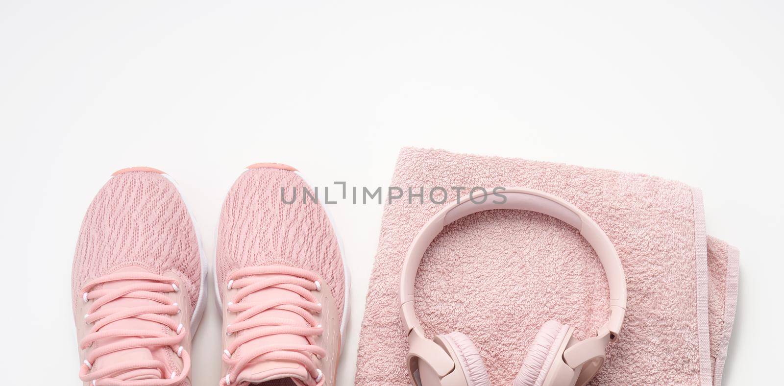 pair of pink textile sneakers, wireless headphones and a textile pink towel on a white background. Set for sports, running