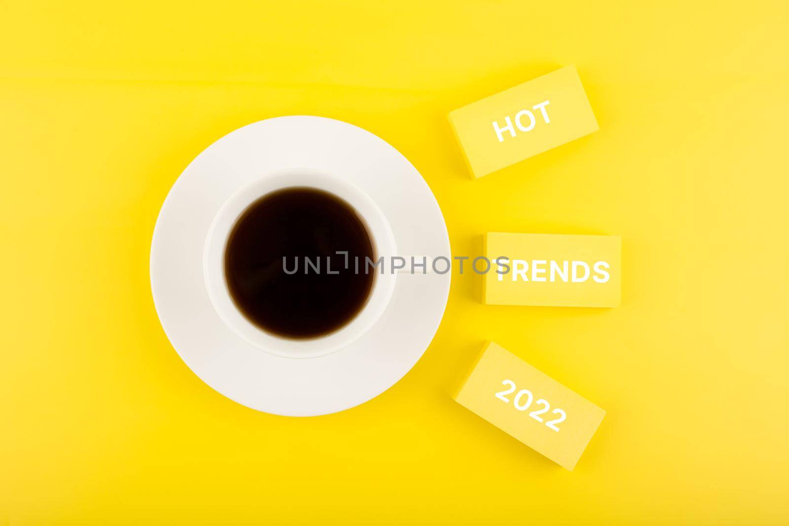 Hot trends 2022 written on rectangles next to cup of coffee on bright yellow background by Senorina_Irina