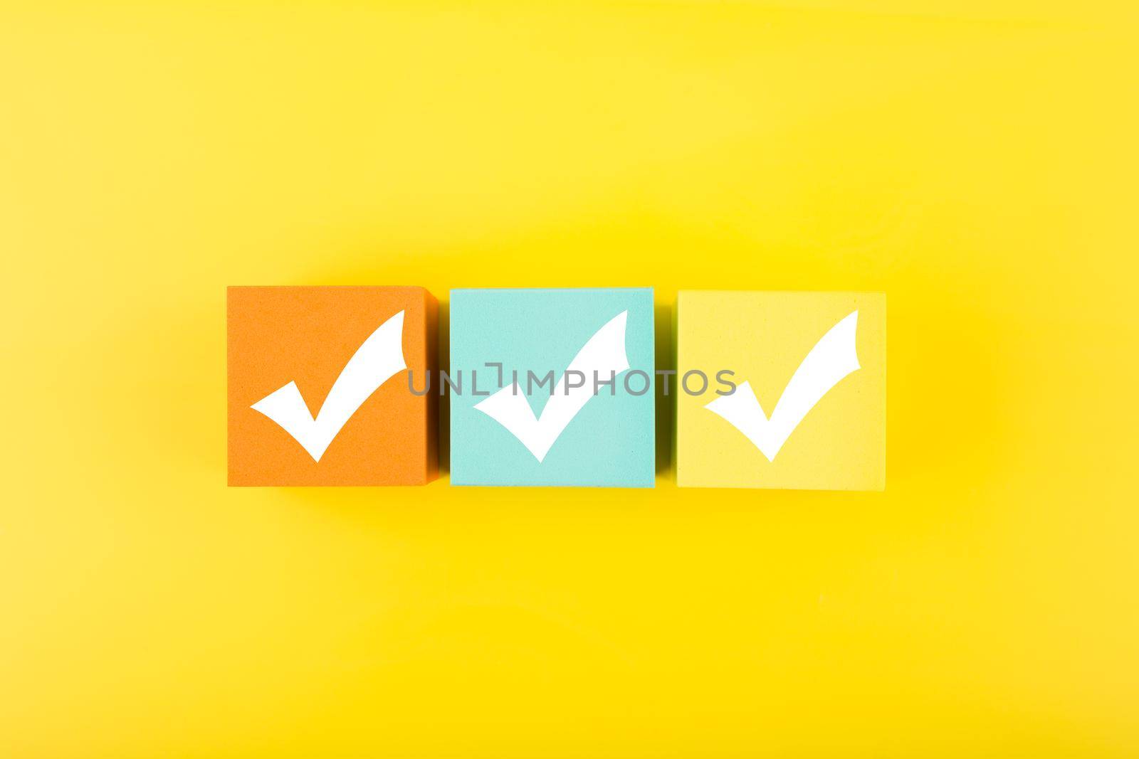 Three checkmarks on colorful blocks against bright yellow background by Senorina_Irina