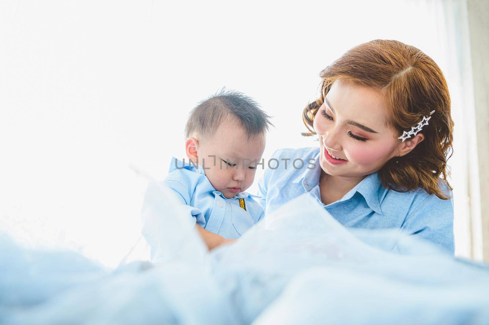 Asian mother and her son wearing blue shirts on bed in bedroom with copy space at home. People lifestyle and Newborn medical concept. State quarantine in Covid-19 or Coranavirus epidemic theme