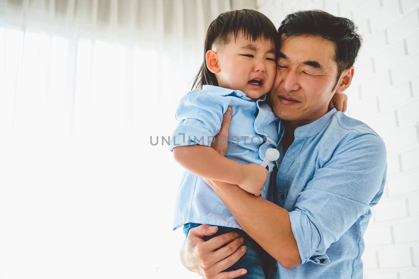 Asian Japanese father carrying and consoling his crying son in bedroom at his home with window and white curtain background. People lifestyle health. Quarantine in Covid-19 or Coranavirus epidemic
