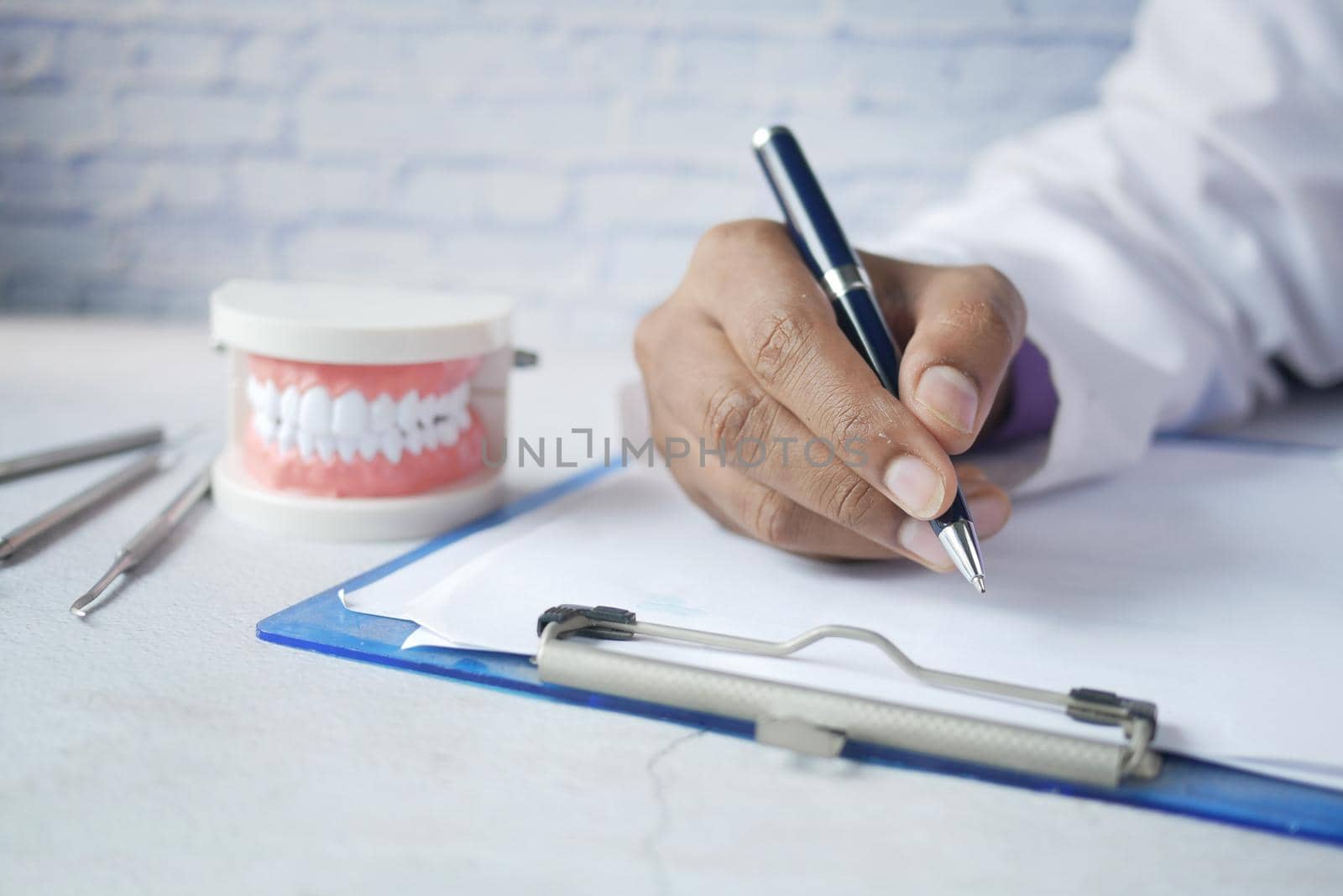 doctor hand writing prescription with plastic dental teeth model on table by towfiq007