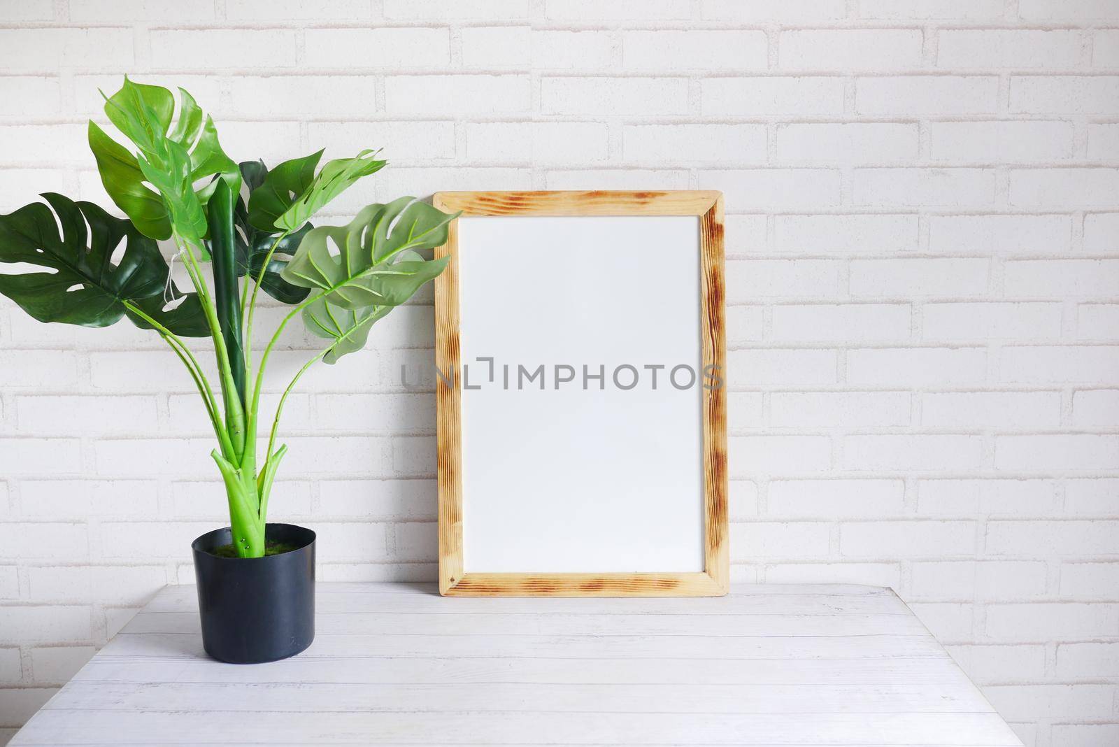 Black frame mockup on table against white wall, by towfiq007