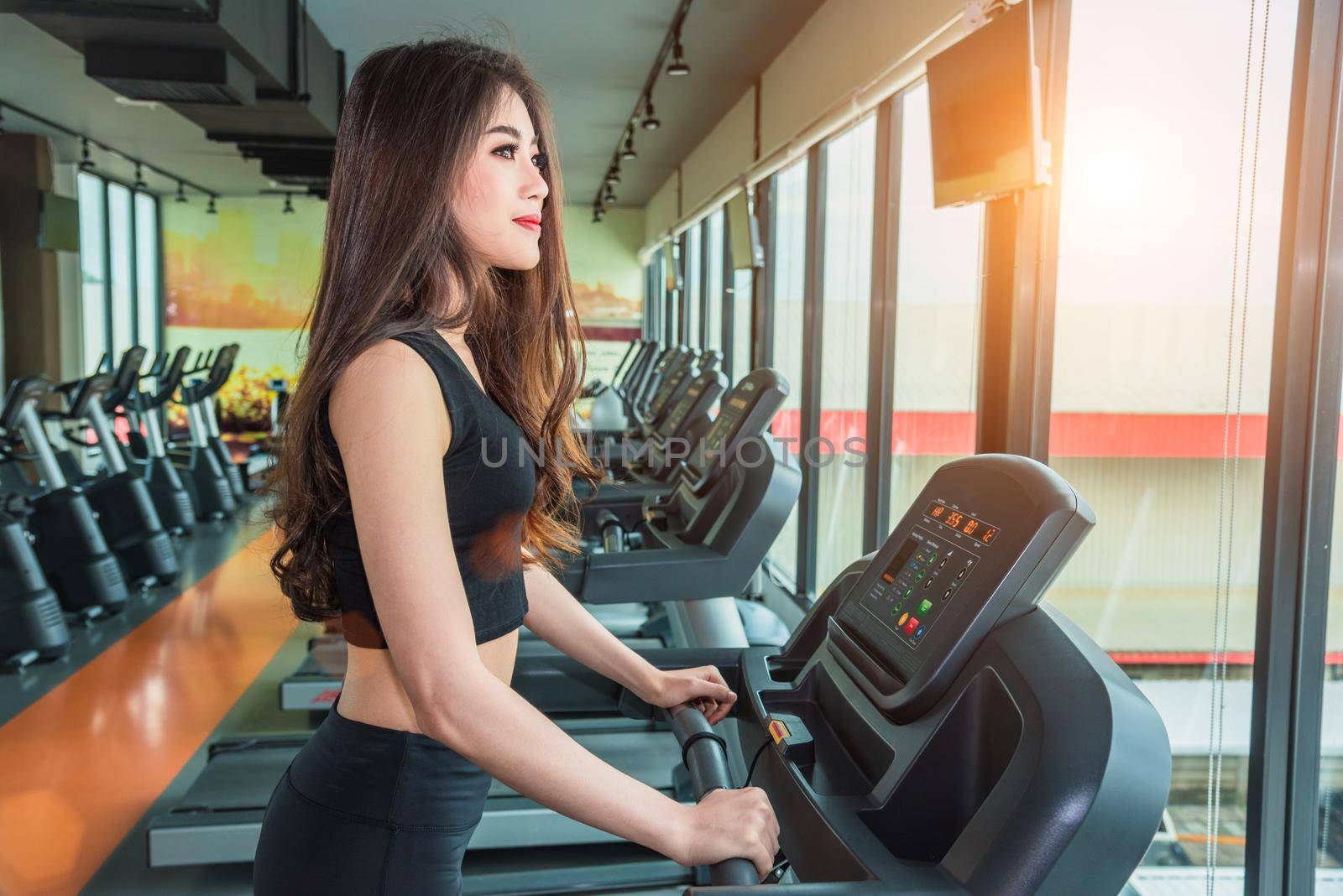 Asian sport woman walking or running on treadmill equipment in fitness workout gym. Sport and Beauty concept. Workout and Strength Training theme. Cardio and Diet theme