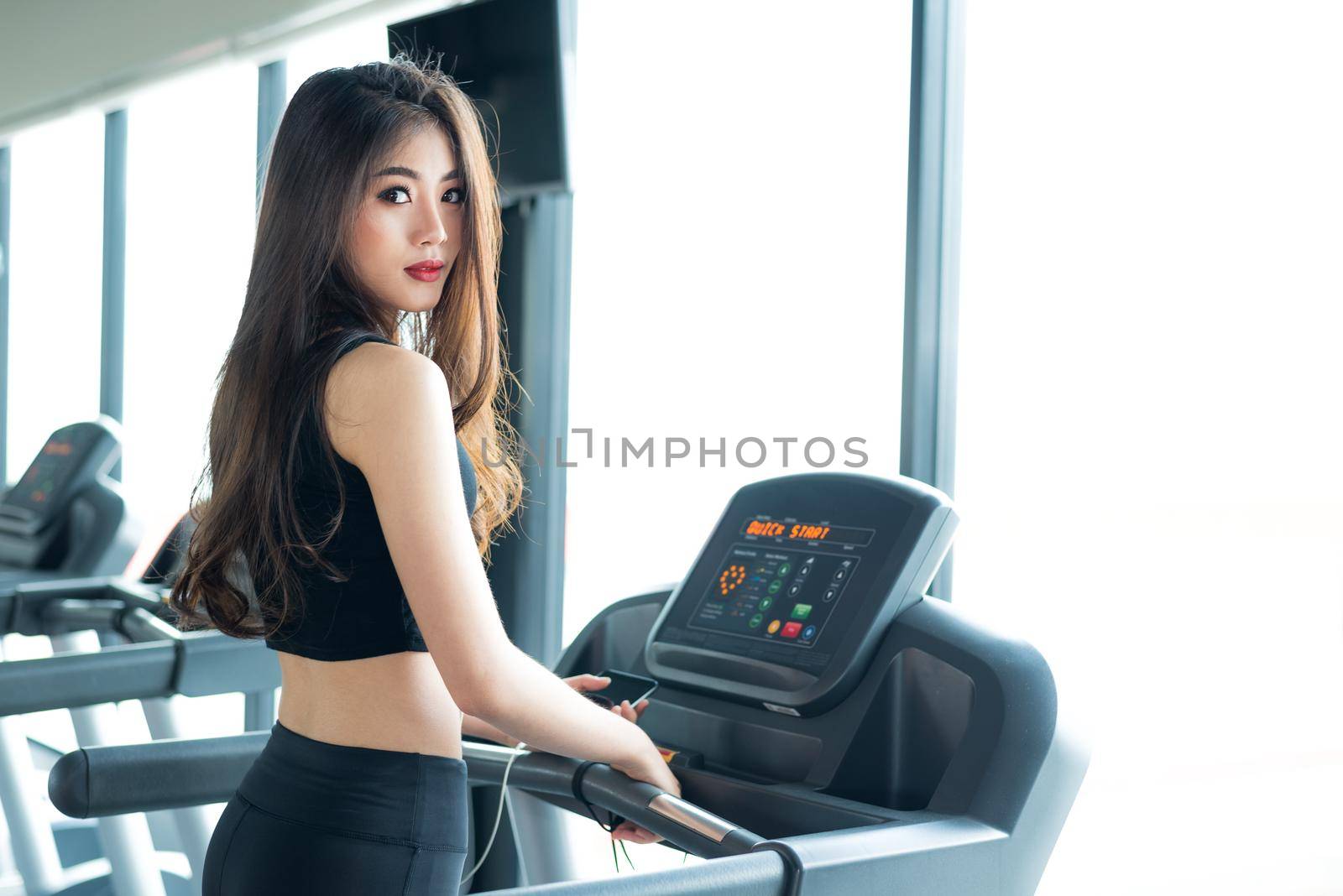 Asian sport woman walking or running on treadmill equipment in fitness workout gym. Sport and Beauty concept. Workout and Strength Training theme. Cardio and Diet theme. Woman portrait