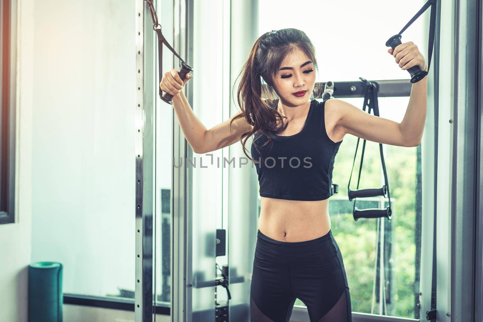 Asian young woman doing elastic rope exercises at cross fitness gym. Strength training and muscular. Beauty and Healthy concept. Sport equipment and Sport club center theme. 