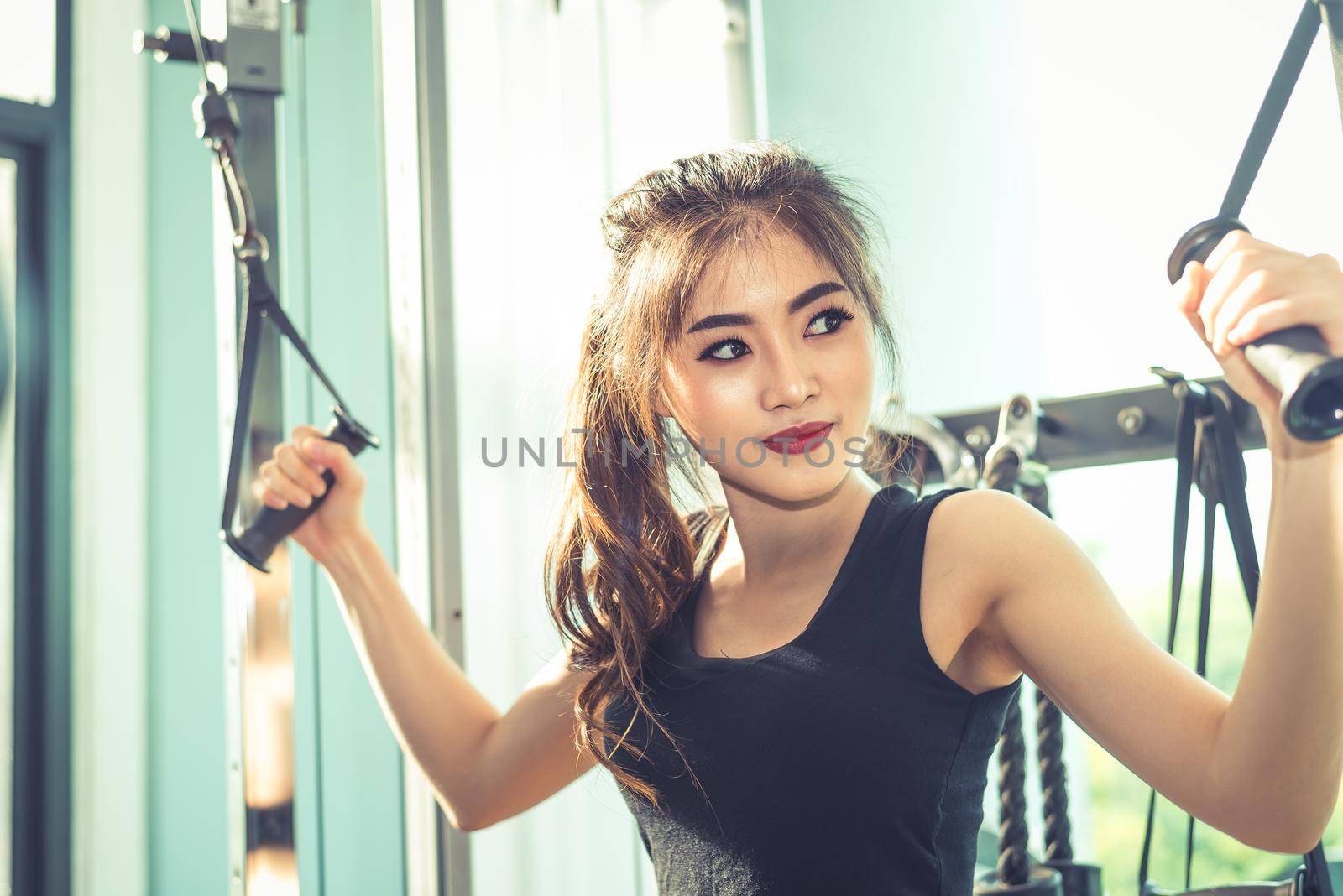 Asian young woman doing elastic rope exercises at cross fitness gym. Strength training and muscular. Beauty and Healthy concept. Sport equipment and Sport club center theme. 