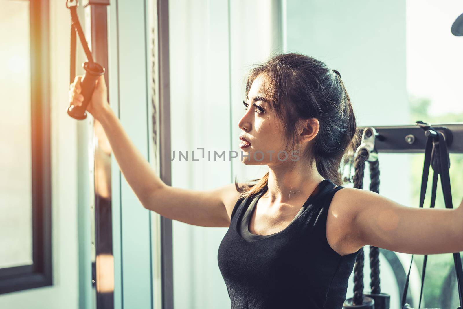 Asian young woman doing elastic rope exercises at cross fitness gym. Strength training and muscular. Beauty and Healthy concept. Sport equipment and Sport club center theme.  by MiniStocker