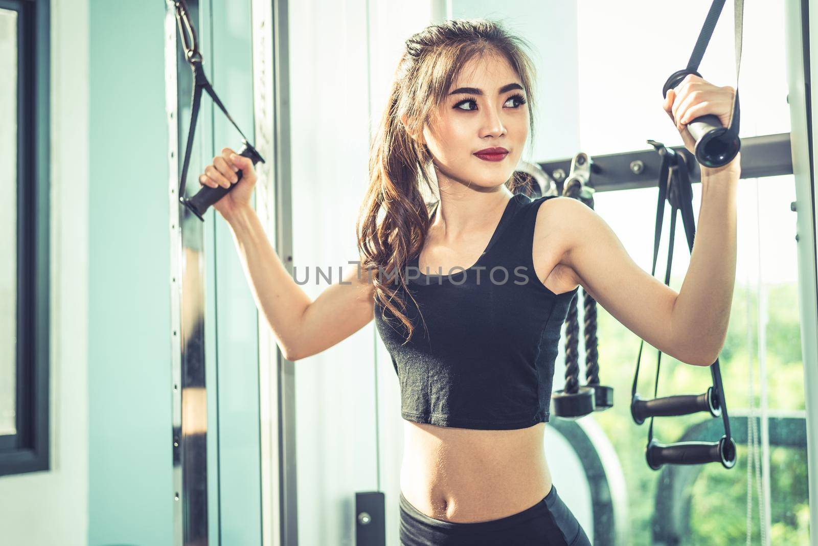 Asian young woman doing elastic rope exercises at cross fitness gym. Strength training and muscular. Beauty and Healthy concept. Sport equipment and Sport club center theme. 