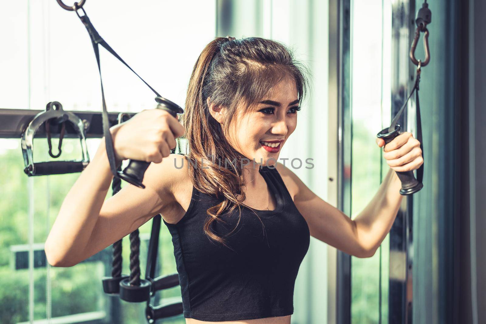 Asian young woman doing elastic rope exercises at cross fitness gym. Strength training and muscular. Beauty and Healthy concept. Sport equipment and Sport club center theme.  by MiniStocker