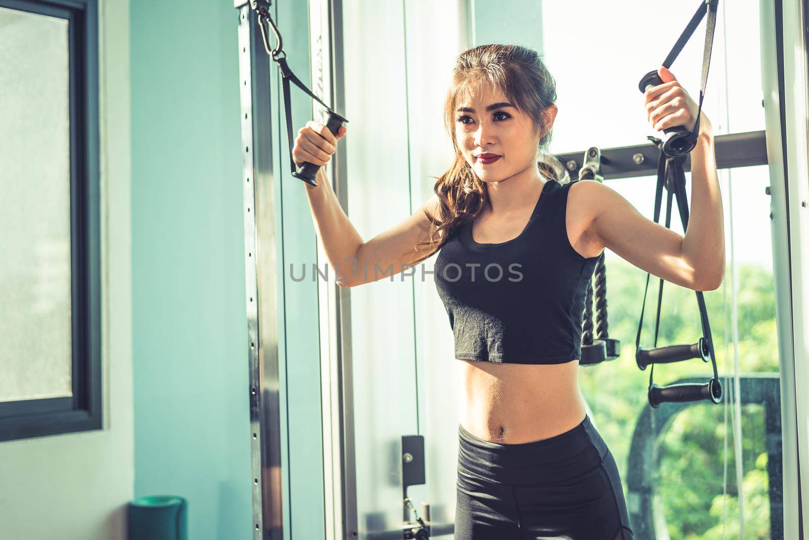 Asian young woman doing elastic rope exercises at cross fitness gym. Strength training and muscular. Beauty and Healthy concept. Sport equipment and Sport club center theme. 