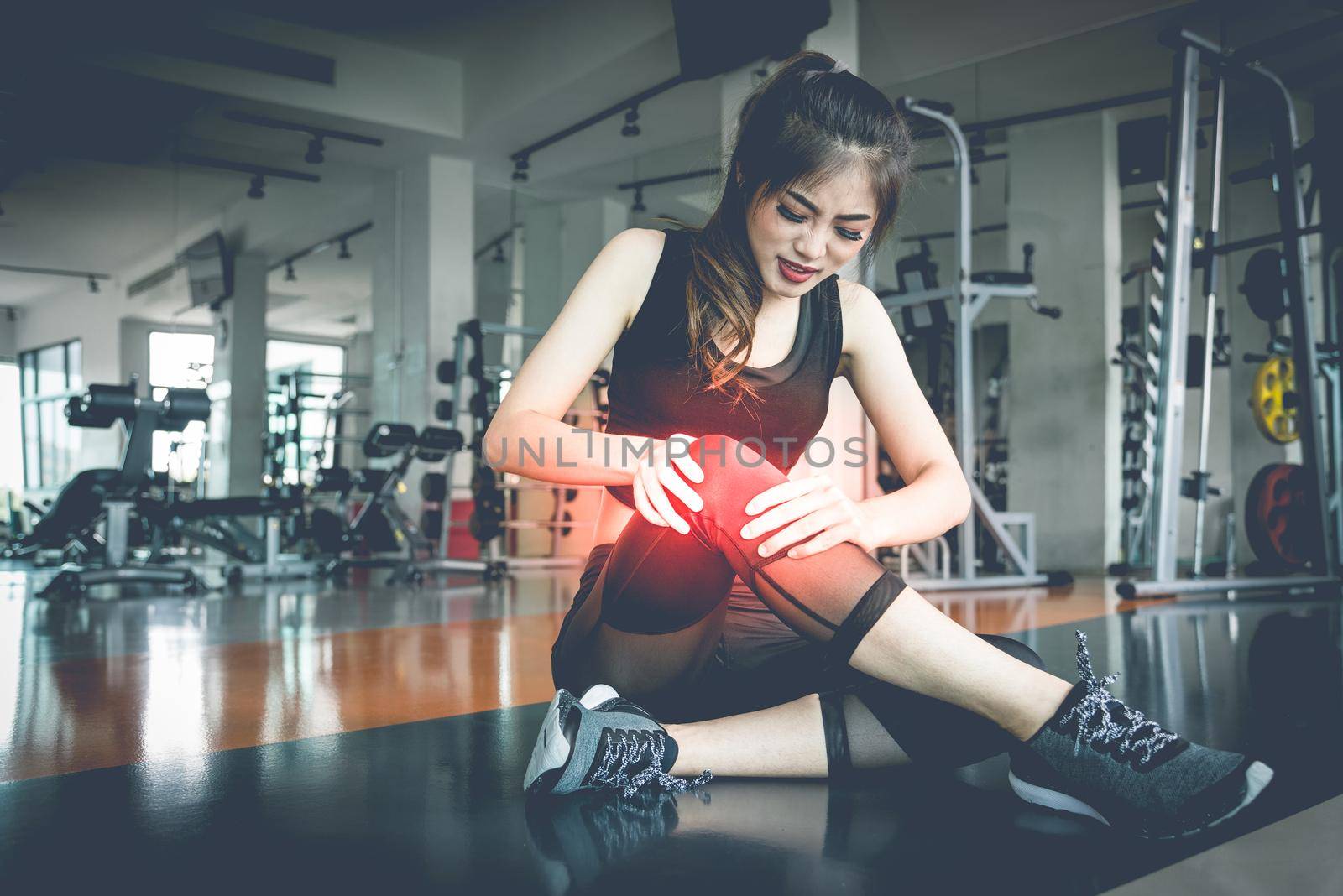 Asian woman injuries during workout at knee in fitness gym. Medical and Healthcare concept. Exercise and Training theme.  by MiniStocker