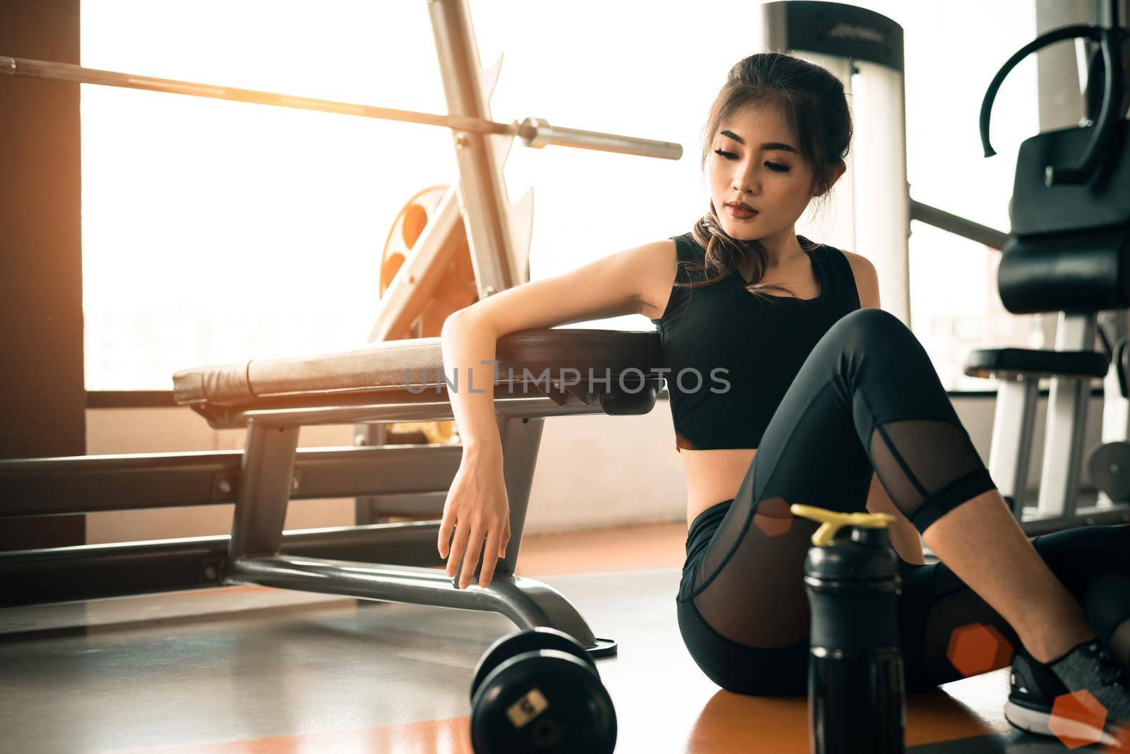 Asian young woman relaxing in fitness gym and sport club center with equipment and dumbbell. Workout and Strength training concept. Beauty and Healthy theme. Gymnasium background