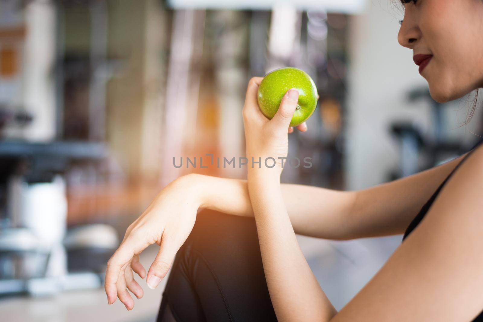 Sports woman sitting and eating green apple in fitness training gym. Food and Fruit and nutrition concept. Relax and Clean food concept. Healthcare and workout exercise theme. 