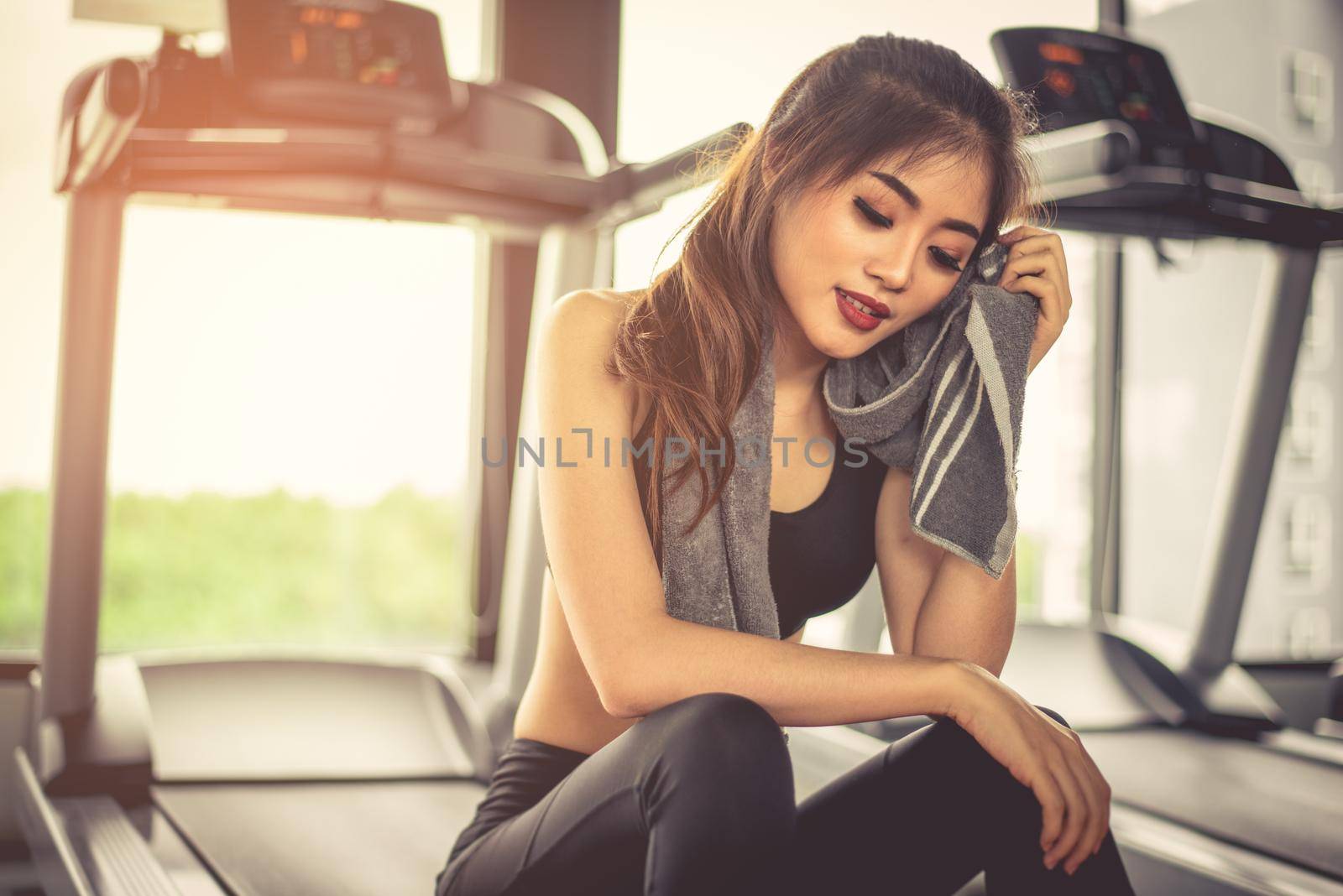 Woman sweats by towel during rest in fitness gym with fitness running equipment. Beauty and relax concept. Gym and fitness training theme  