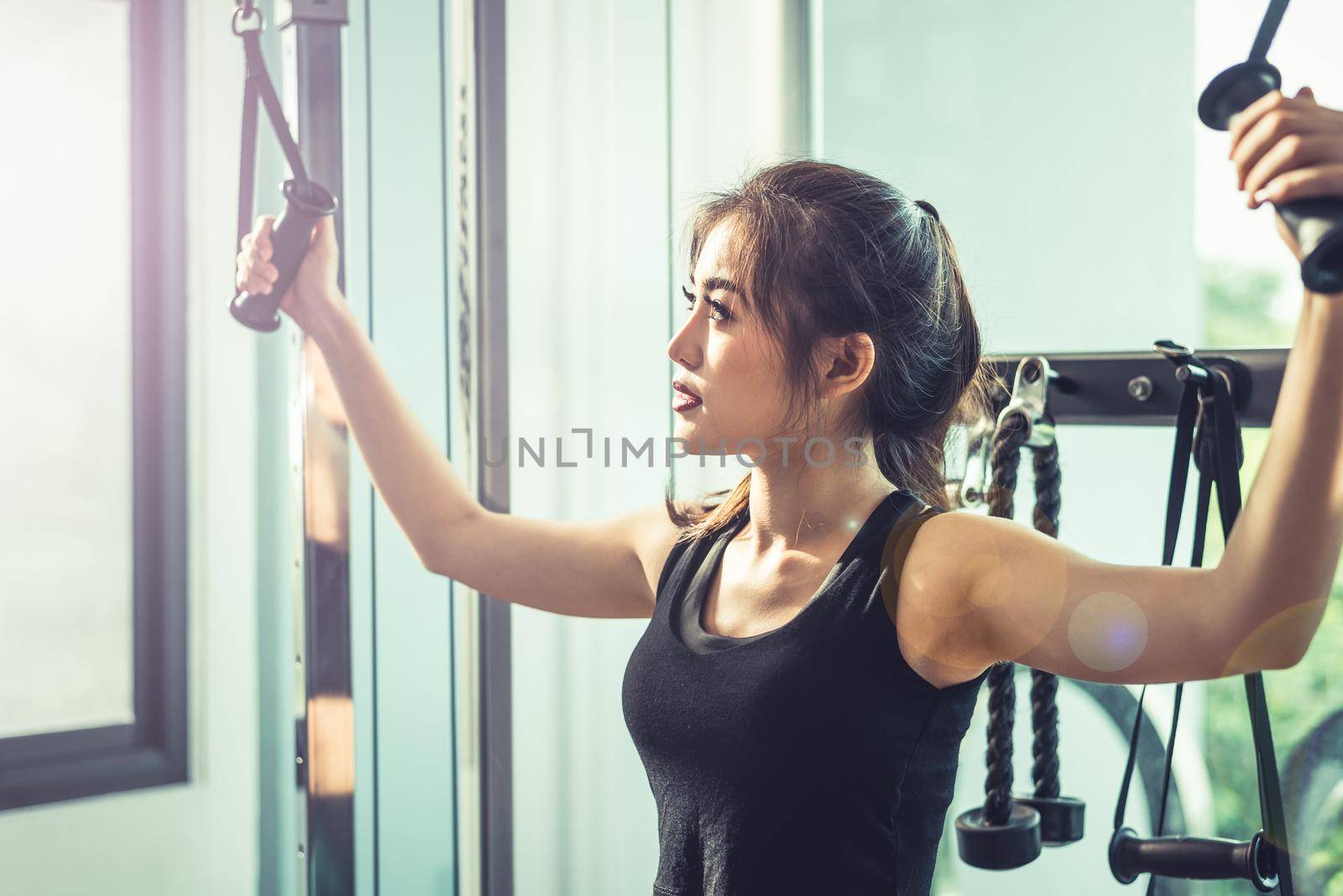 Asian young woman doing elastic rope exercises at cross fitness gym. Strength training and muscular Beauty and Healthy concept. Sport equipment and Sport club center theme.  by MiniStocker