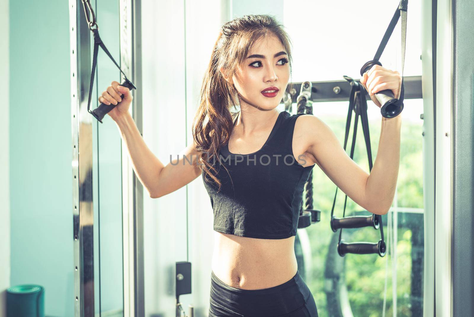 Asian young woman doing elastic rope exercises at cross fitness gym. Strength training and muscular. Beauty and Healthy concept. Sport equipment and Sport club center theme.  by MiniStocker