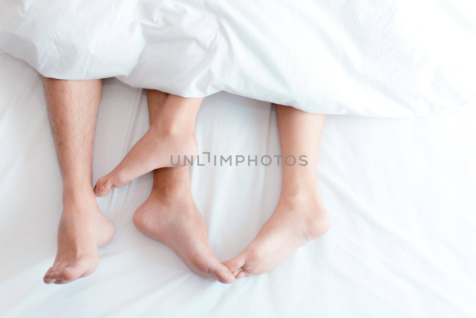 Closeup feet of couple on the bed. Man and woman lovers make love under the blanket or bed sheet. Sex on vacation theme. Valentine and Honeymoon concept. by MiniStocker