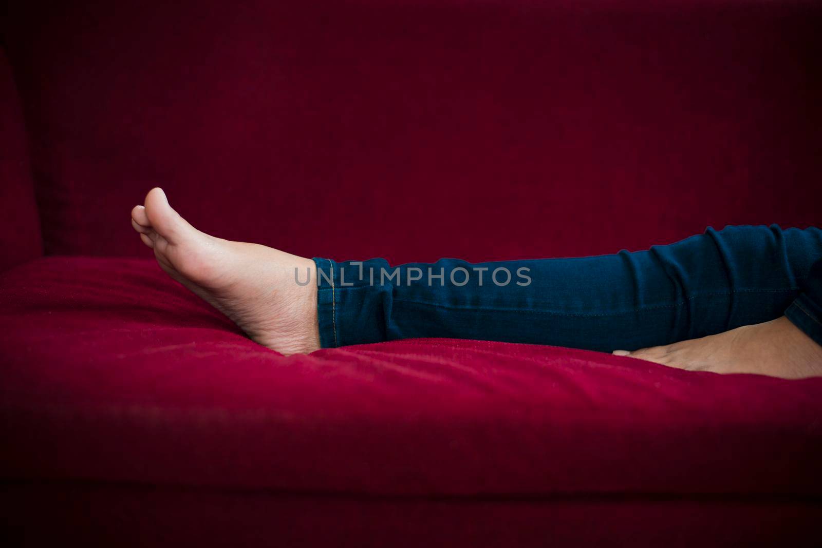 Woman legs with wearing jeans while relaxing at movie theater or home at the red sofa, Relax and holiday concept, Bed time sleeping concept by MiniStocker