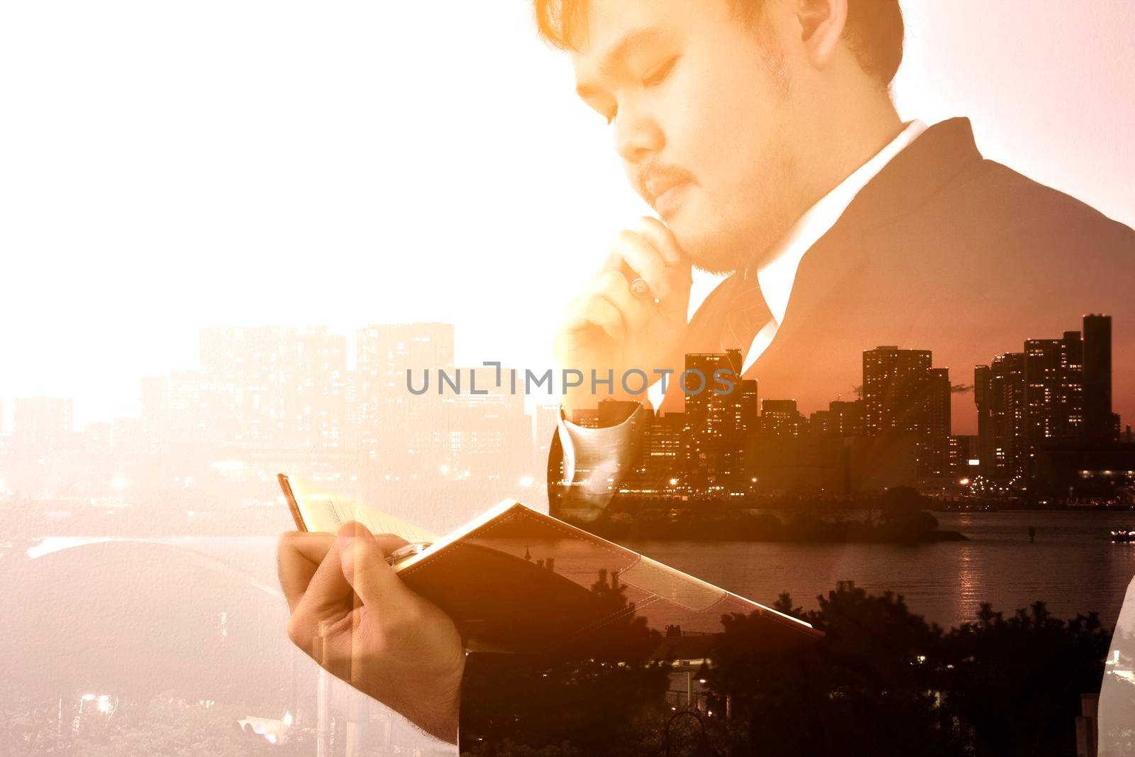 Businessman looking memo and Thinking for idea with big city or town in background,Double exposure, panoramic view contemporary megalopolis background, orange sun light, business concept