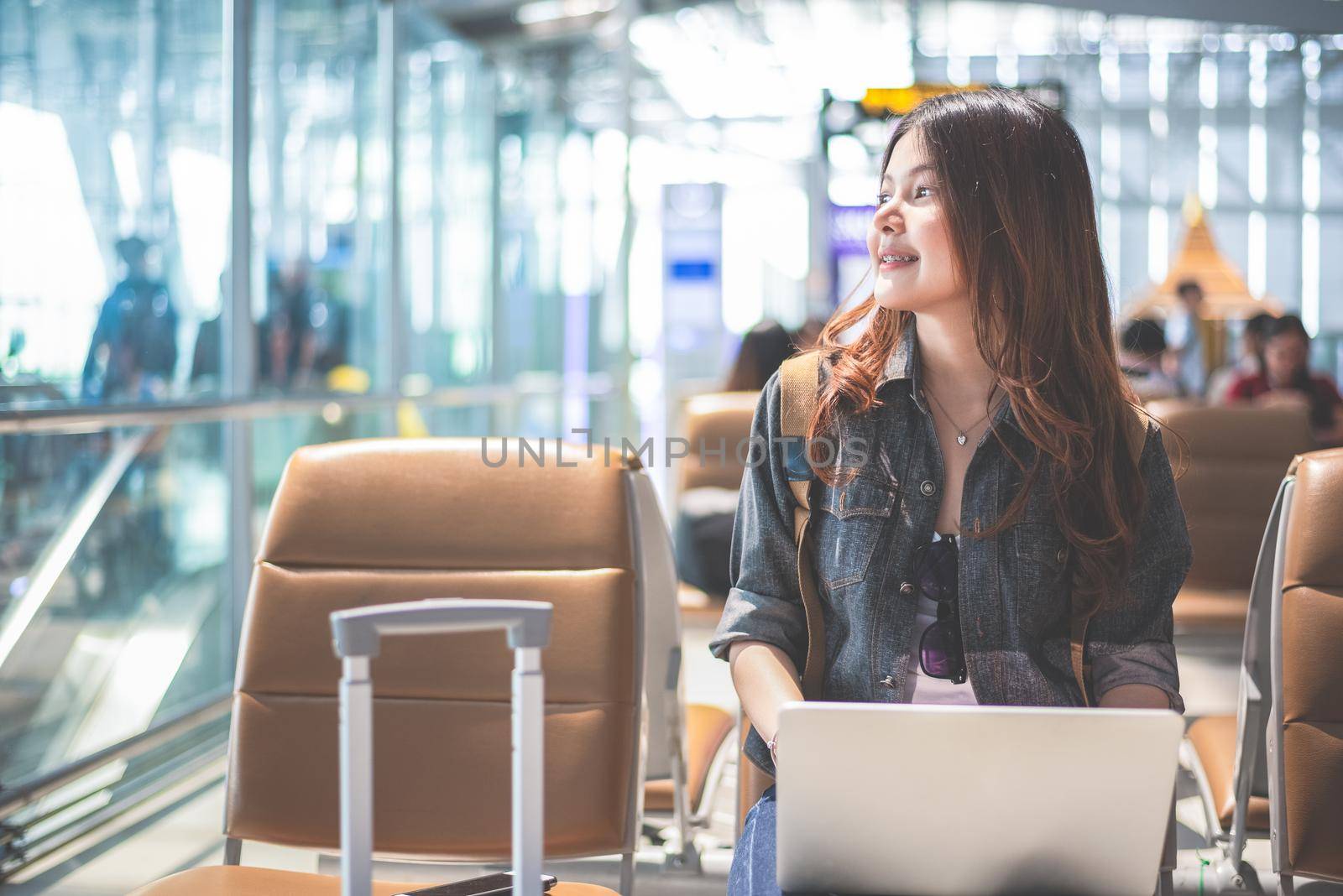 Beauty Asian woman using laptop and looking outside at airport. Woman sitting in airport terminal. People and lifestyle concept. Technology and travel theme. Business and Portrait theme. by MiniStocker