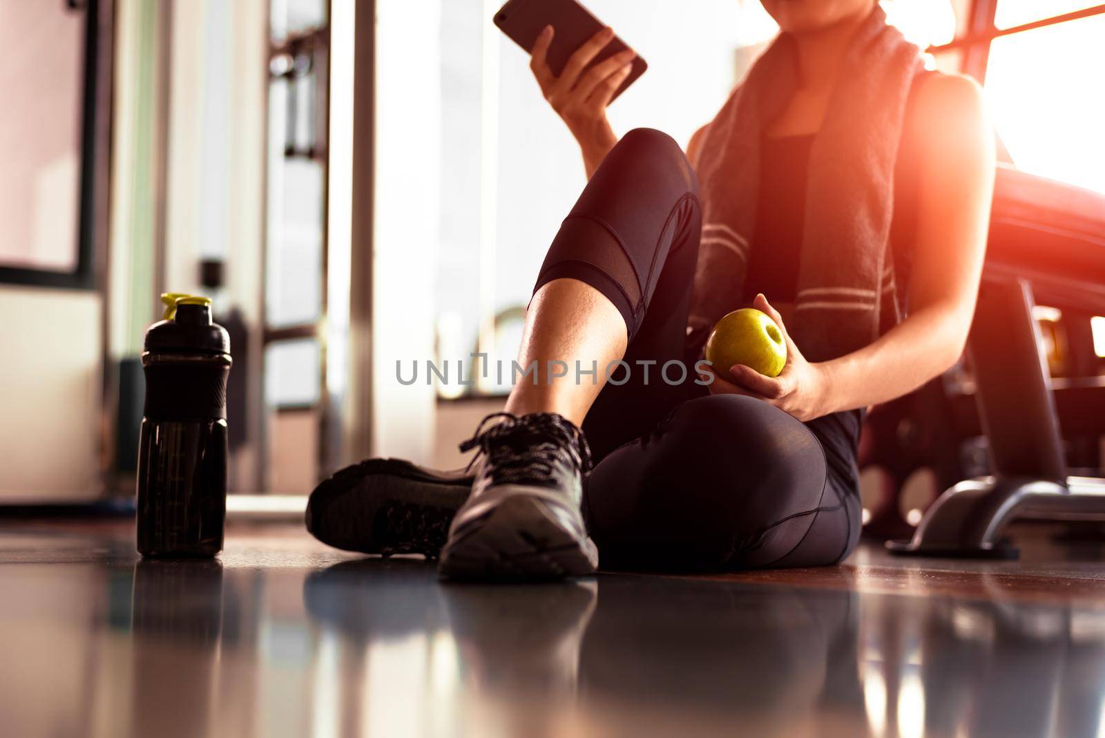 Close up of woman using smart phone and holding apple while workout in fitness gym. Sport and Technology concept. Lifestyles and Healthcare theme.