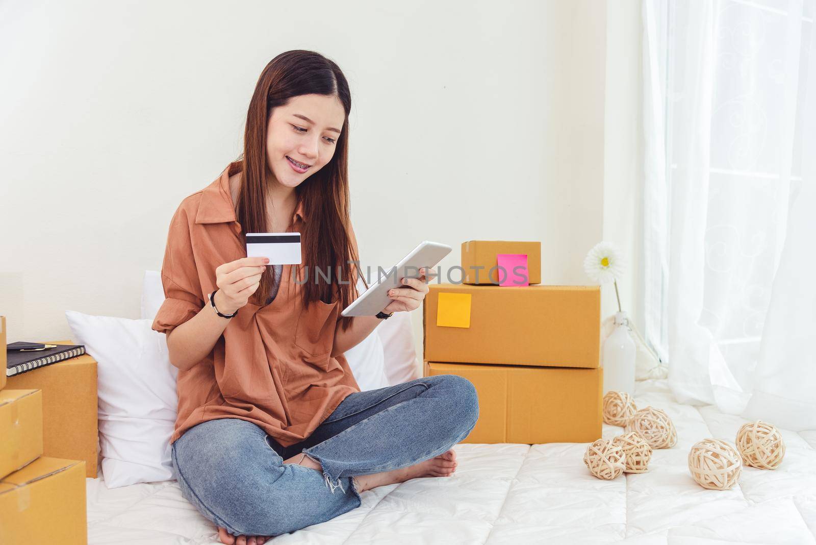 Beauty Asian woman using tablet and credit card. Start up small business entrepreneur SME and checking order list in bedroom, Young happy freelance woman shopping online marketing or sending parcel