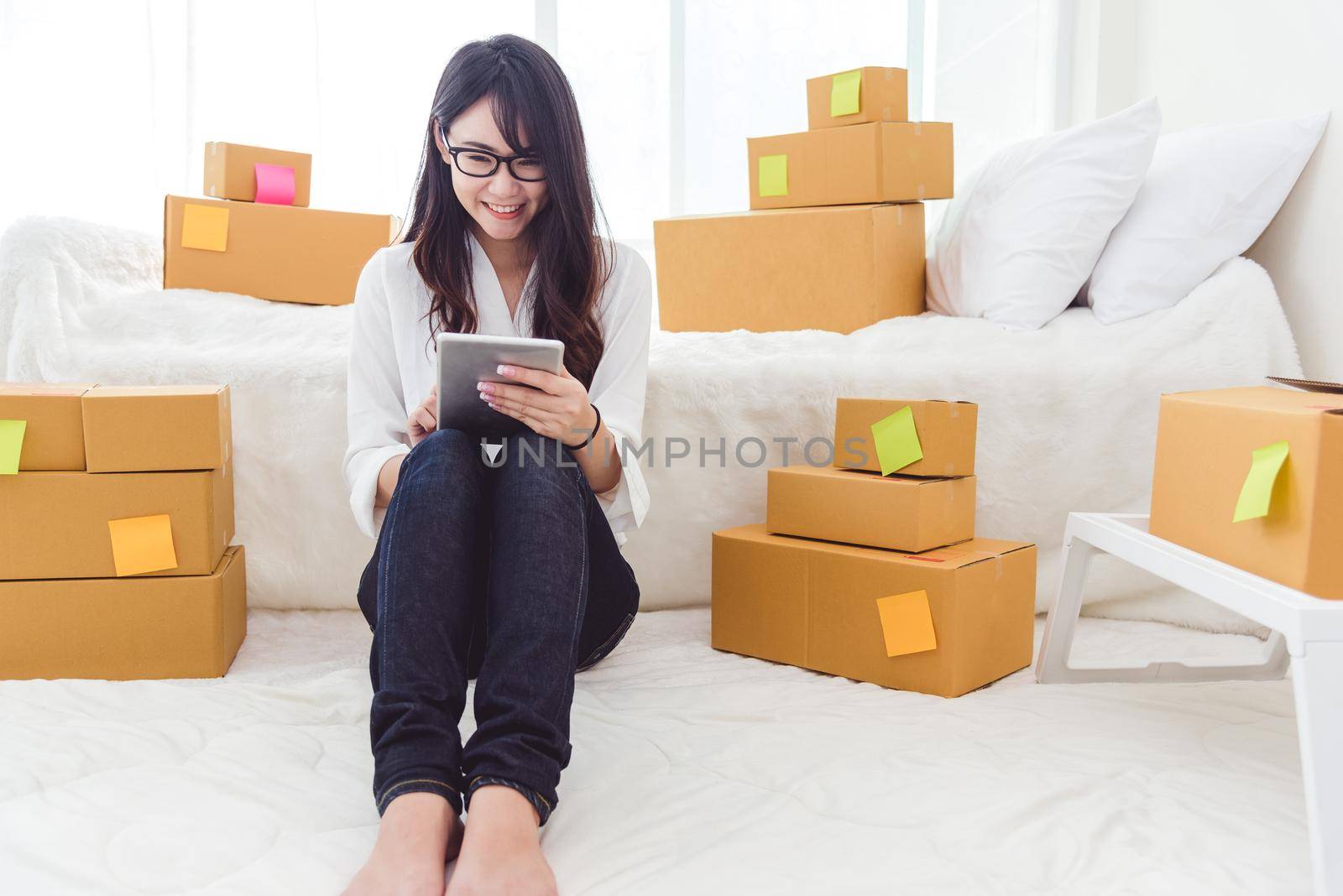 Beauty Asian woman using tablet and start up small business entrepreneur SME and checking order list in bedroom, Young happy freelance woman shopping online marketing or sending parcel to customers