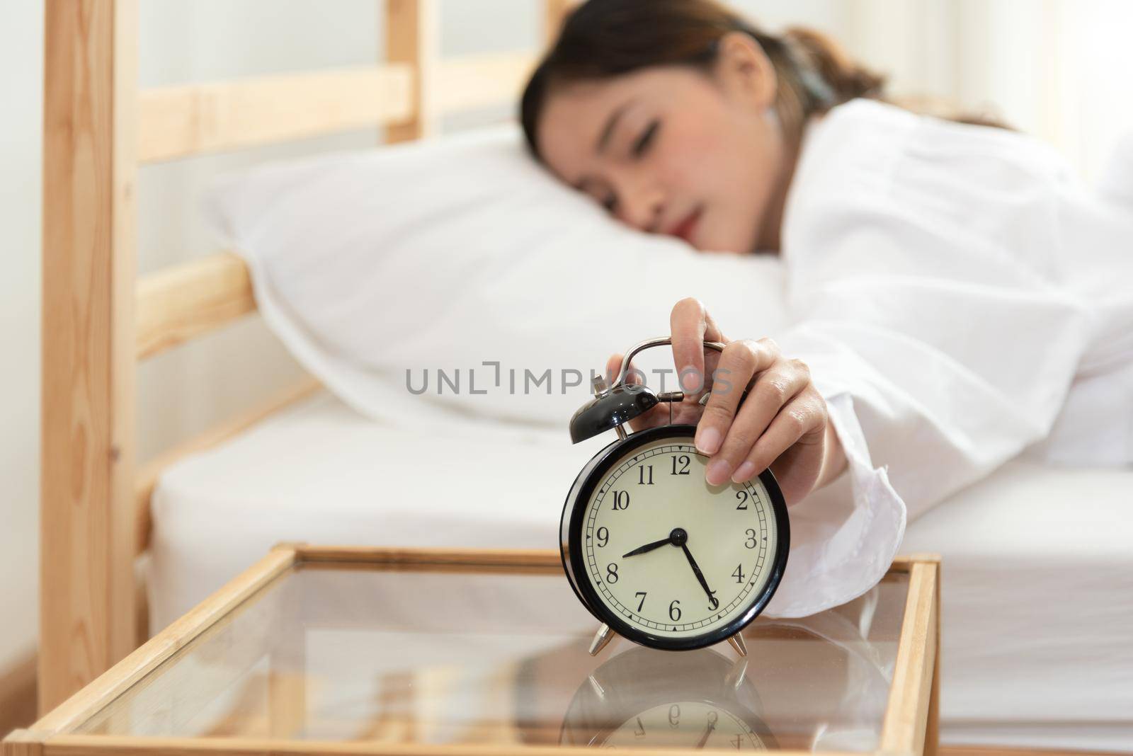 Asian young beauty woman turning off alarm clock in morning late without looking clock and lazy to working on in holiday. Bedroom and bed time concept. Relaxation and people lifestyles of tired worker