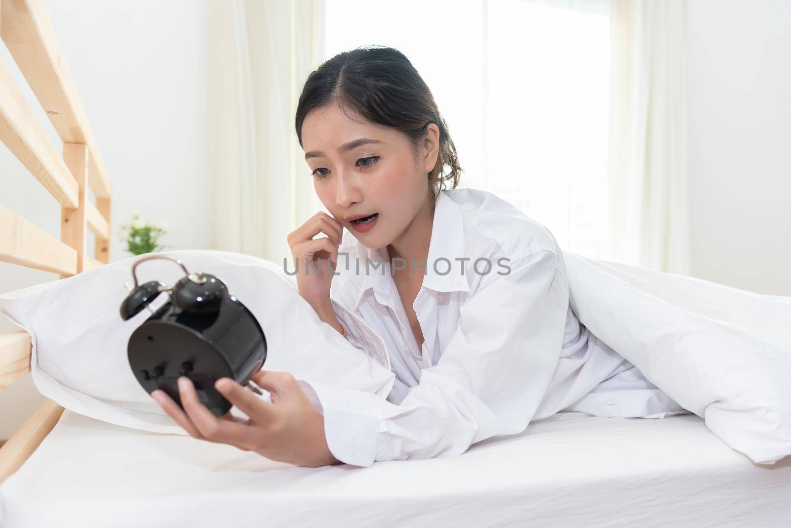 Asian woman shocked when wake up late by forget to setting alarm clock at night and having meeting appointment and working in morning today. People lazy and hurry up rush hour concept. Shocked agape