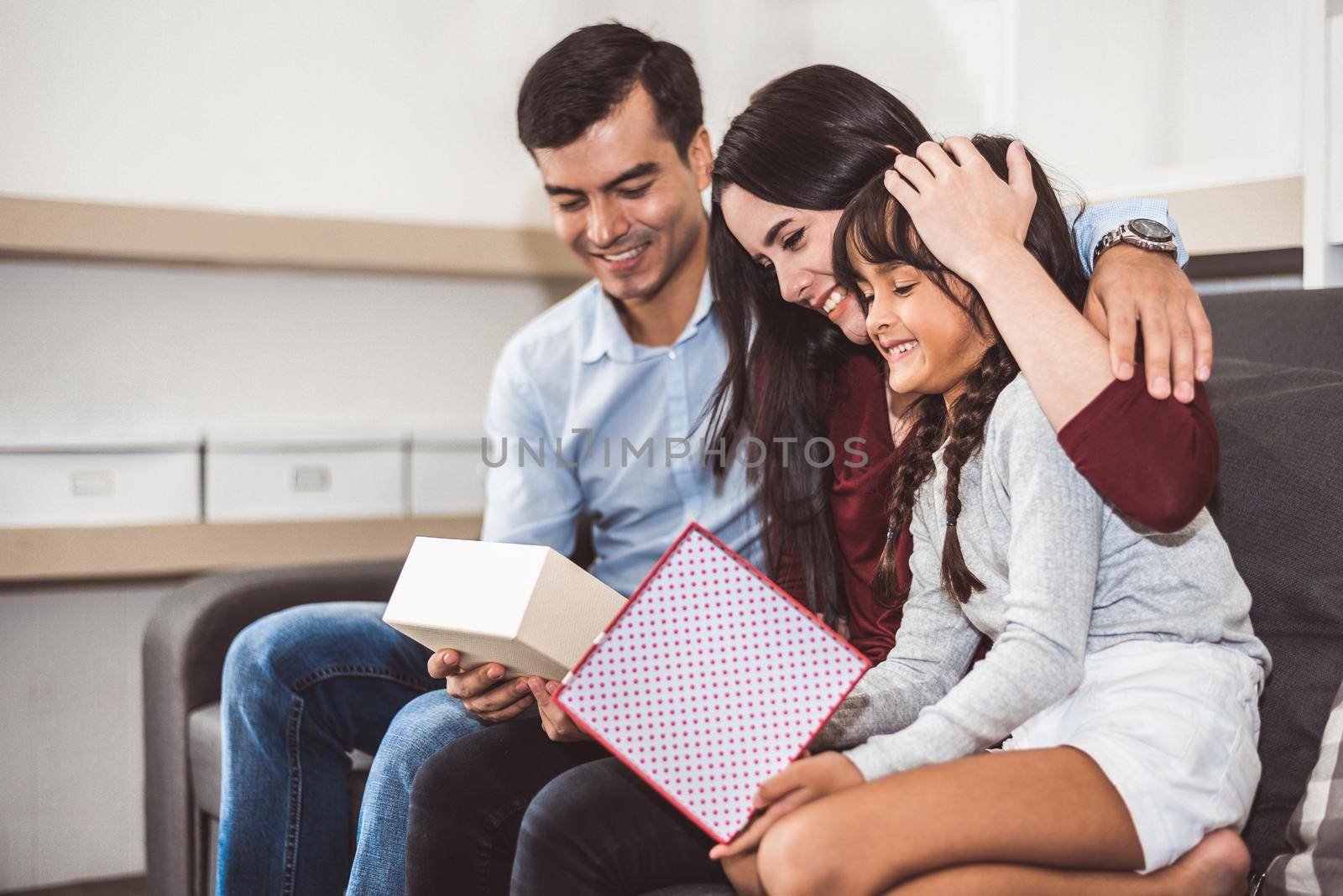 Happy family parents and little girl looking into gift box in Christmas and New year day on sofa in living room. Xmas present for surprised good children in happy home. People and lifestyles concept.