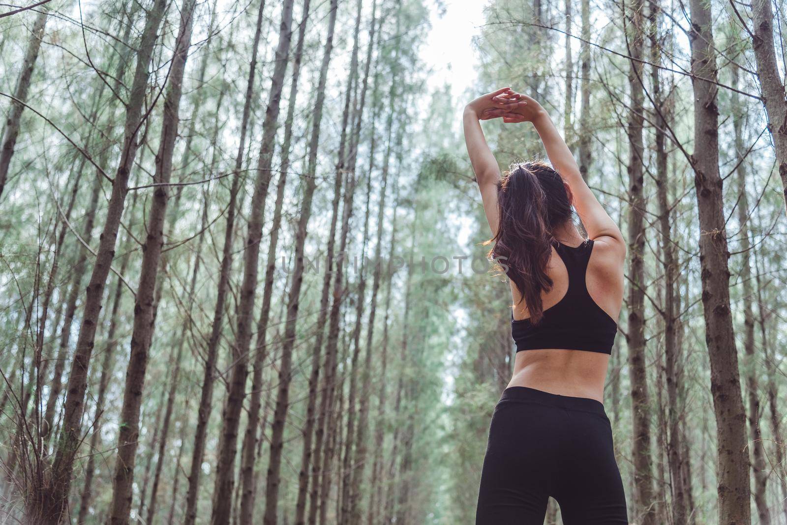 Women stretching arms and breathing fresh air in middle of pinewood forest while exercising. Workouts and Lifestyles concept. Happy life and Healthcare theme. Nature and Outdoors theme. Back view