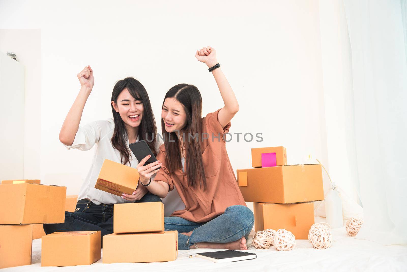 Two young Asian woman startup small business entrepreneur SME distribution warehouse with parcel mail box. Owner home office. Online marketing and product packaging and delivery service. Happy gesture