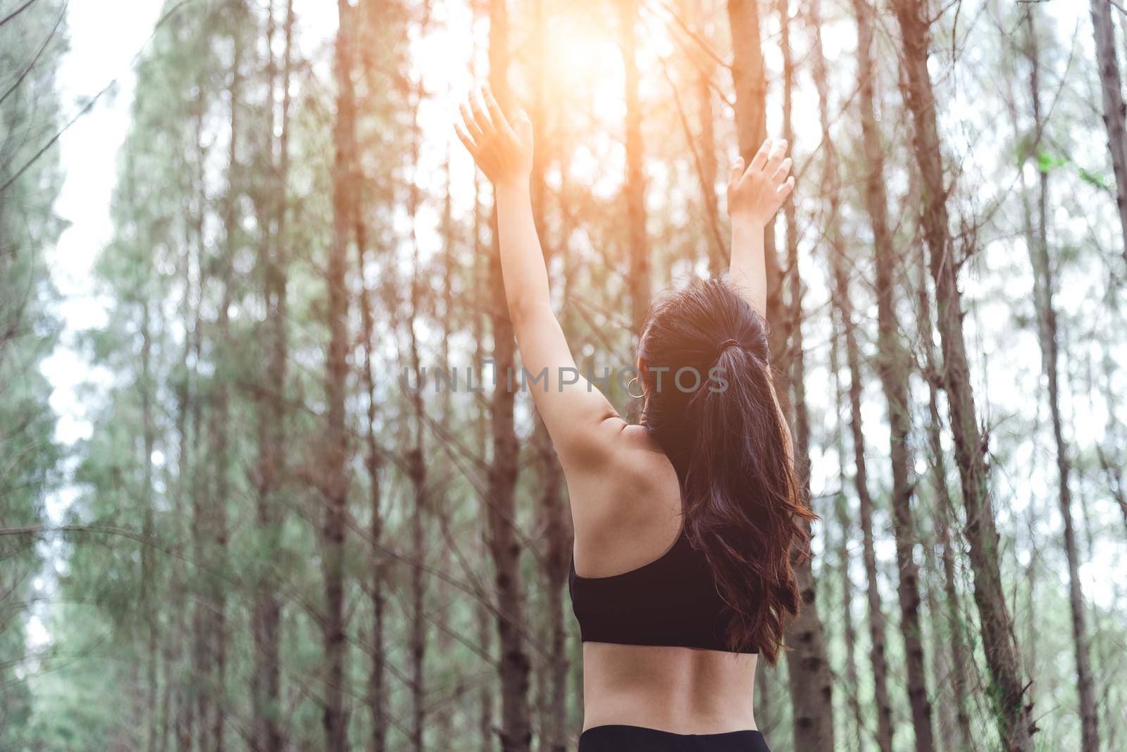 Woman stretching arms and breathing fresh air in middle of pinewood forest while exercising. Workouts and Lifestyles concept. Happy life and Healthcare theme. Nature and Outdoors theme. Back view by MiniStocker
