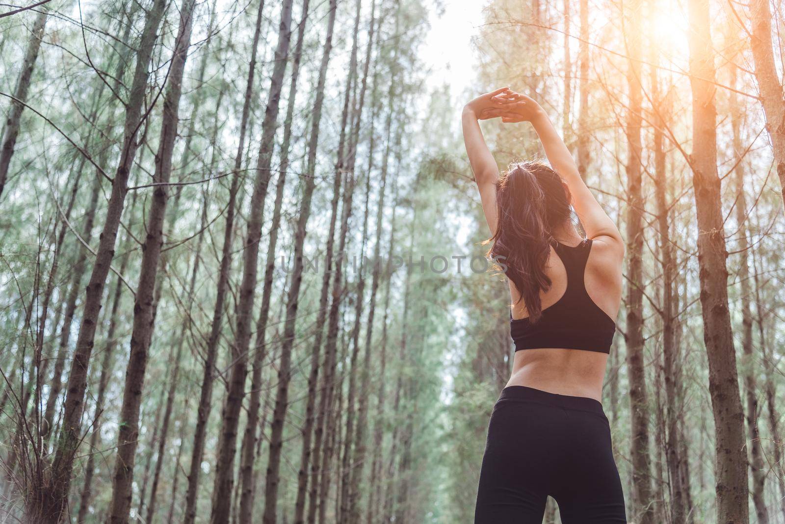 Women stretching arms and breathing fresh air in middle of pinewood forest while exercising. Workouts and Lifestyles concept. Happy life and Healthcare theme. Nature and Outdoors theme. Back view by MiniStocker