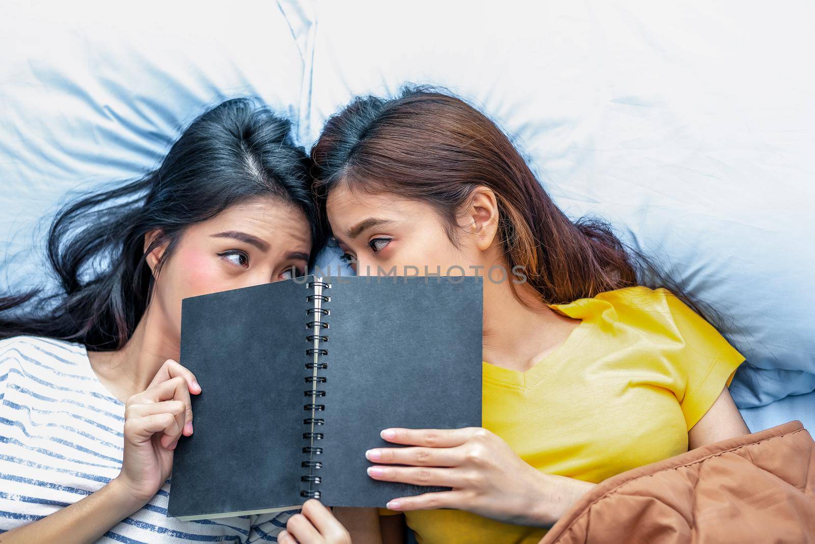 Cute Asian lesbian couple reading book together and lying on bed. Lifestyles and lovers concept. Happiness life and relax theme. by MiniStocker
