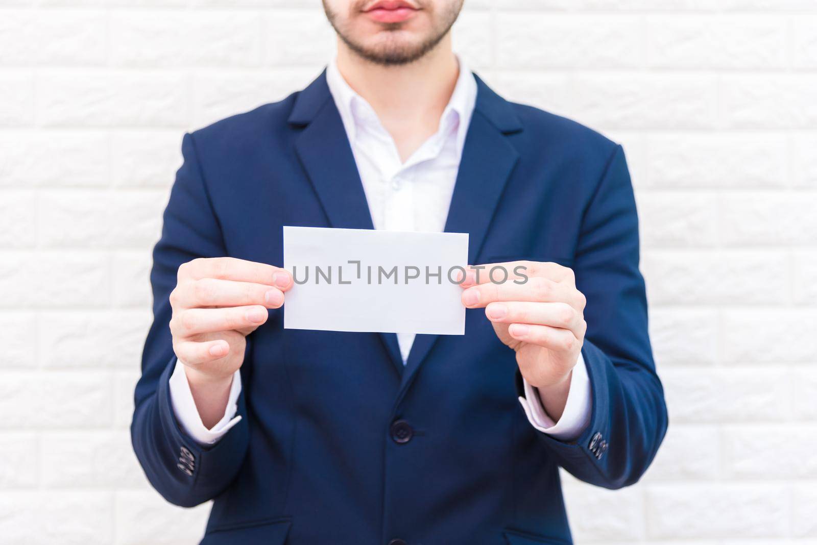 Business man showing white paper. Man  wearing blue suit and holding white blank card. Lifestyle and working concept. Business and object theme. Blank space in paper for insert text. by MiniStocker