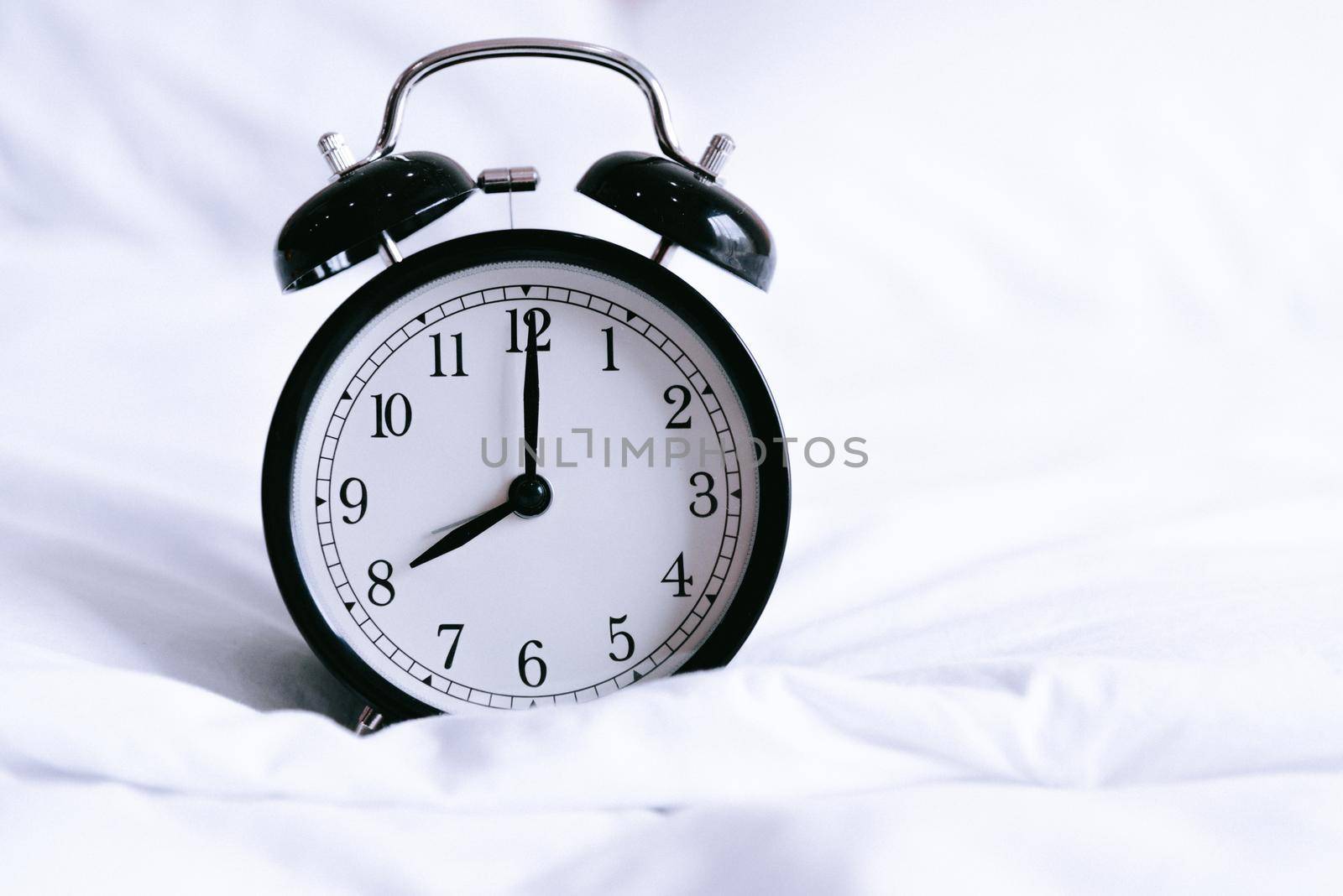 Black alarm clock on white bed. Time and hours concept. Interior and object theme