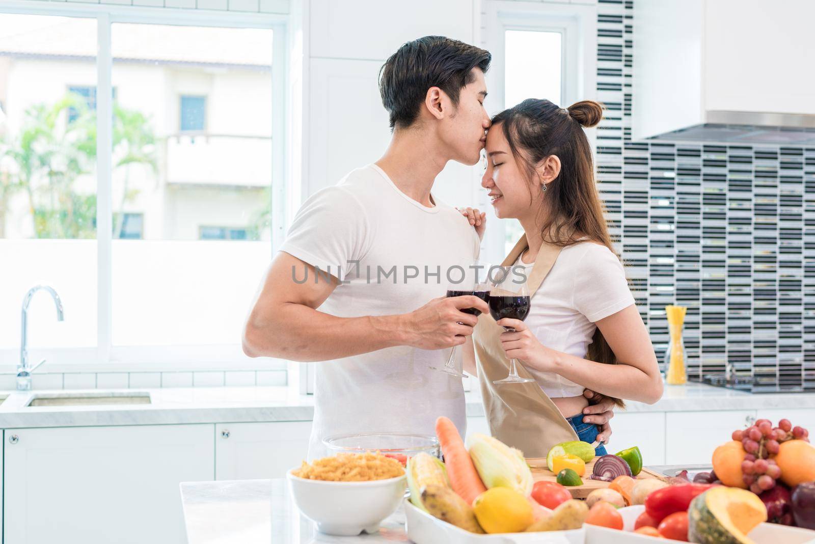 Asian lovers or couples kissing forehead and drinking wine in kitchen room at home. Love and happiness concept Sweet honeymoon and Valentine day theme