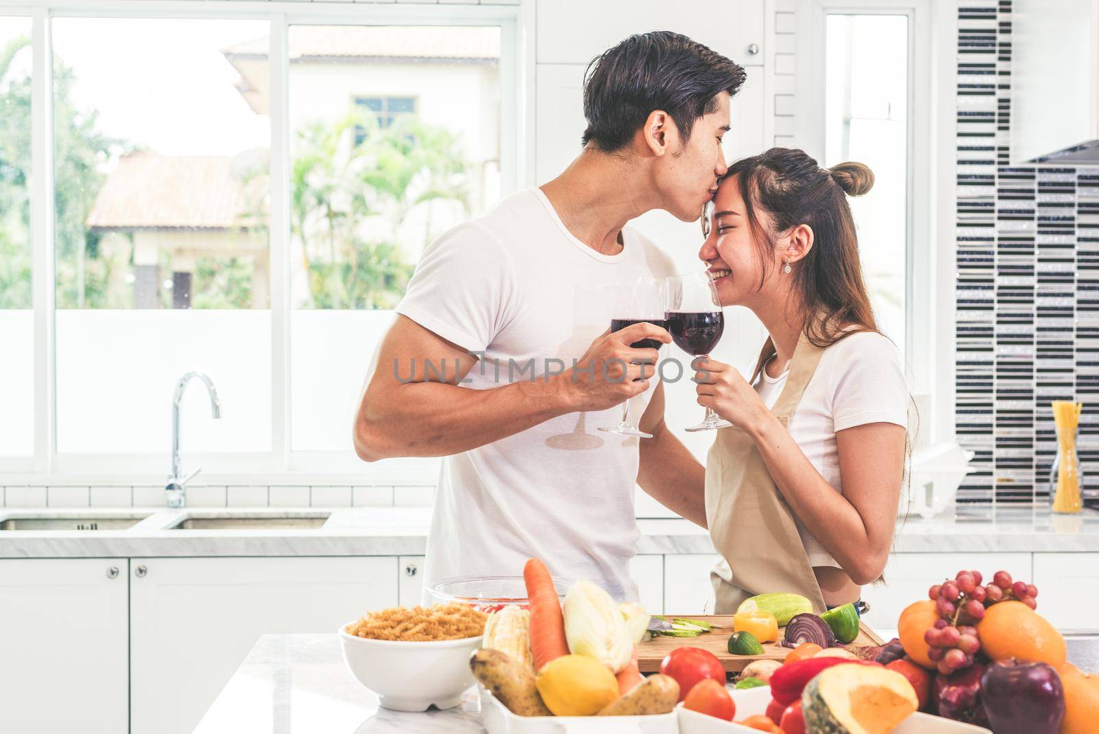 Asian lovers or couples kissing forehead and drinking wine in kitchen room at home. Love and happiness concept Sweet honeymoon and Valentine day theme